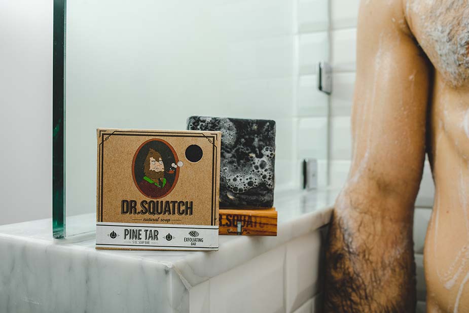 man's torso next to Dr. Squatch soap in shower