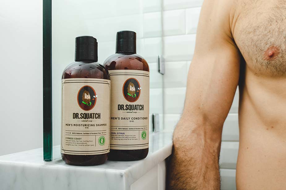 man's torso next to Dr. Squatch hair care kit in shower