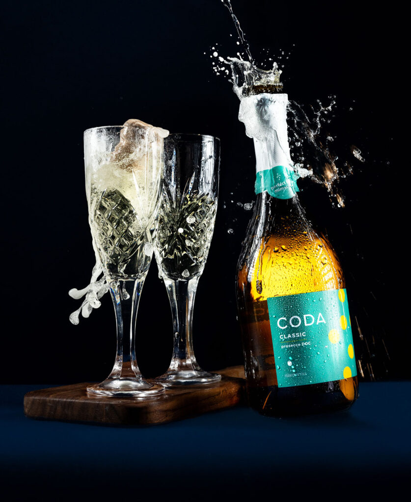 photo of bottle of coda prosecco popping open next to two full flutes of prosecco